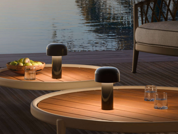 Two glossy black portable lamps illuminating oval wooden tables beside a pool