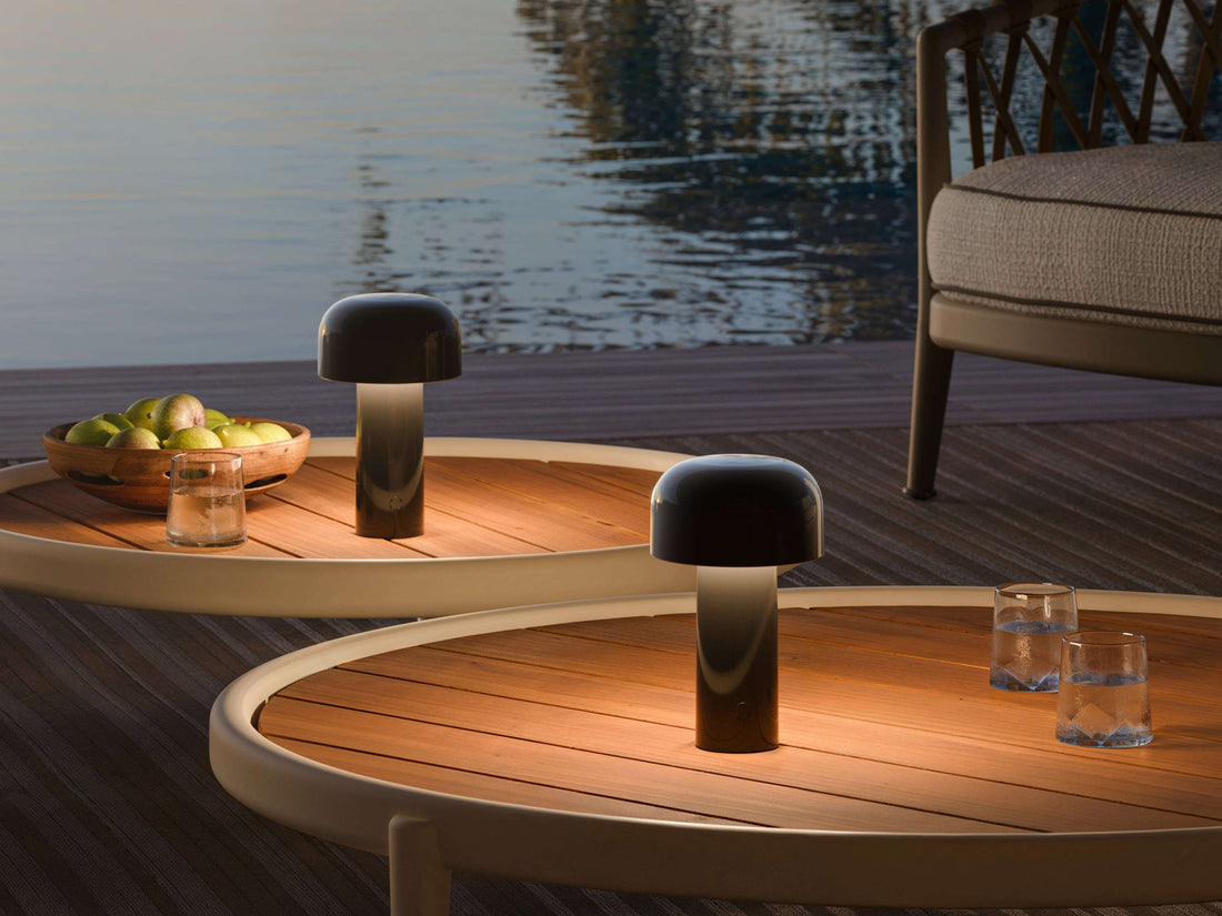 Two glossy black portable lamps illuminating oval wooden tables beside a pool